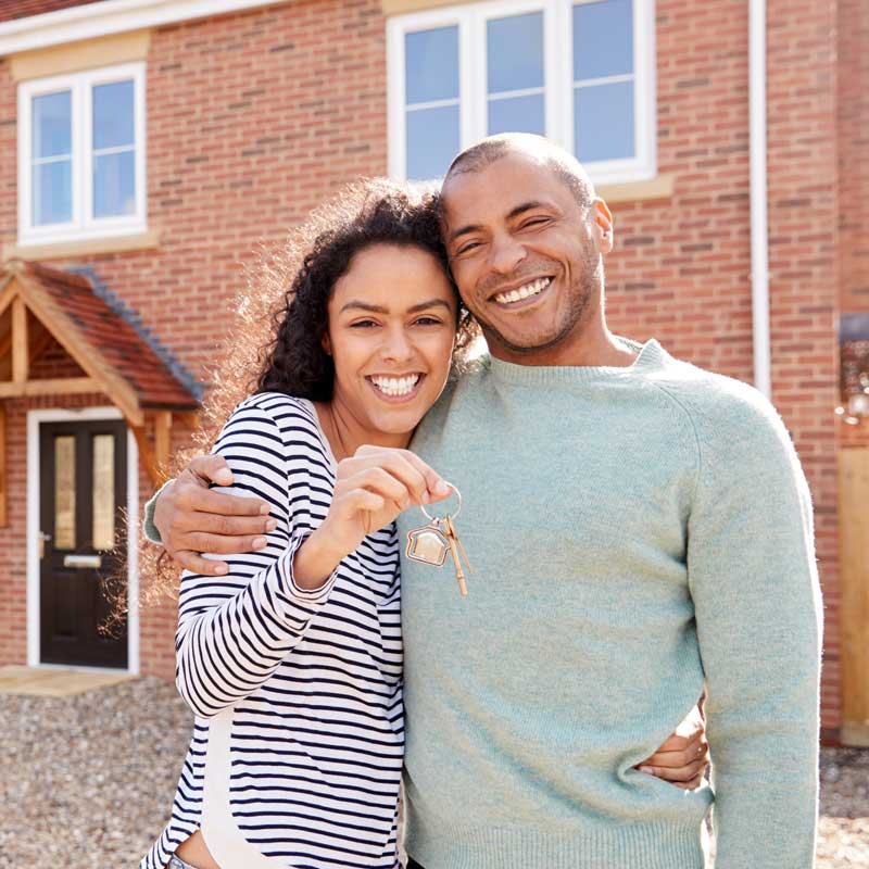 Couple Holding Keys Standing Outside New Home On Moving Day