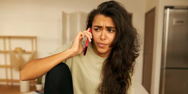 Emotional stylish young female posing indoors talking to customer support operator on phone