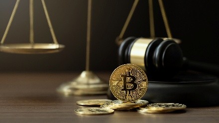A Bitcoin coin rests on a wooden table near scattered coins, a gavel, and scales of justice, symbolizing cryptocurrency regulation and legal balance.