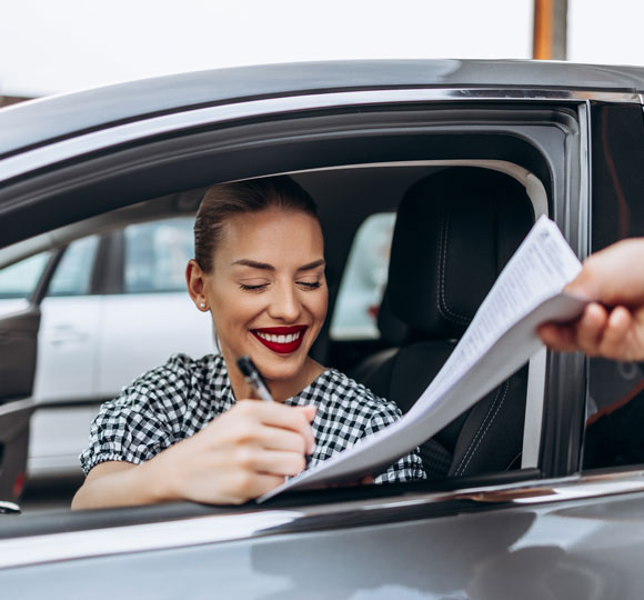 Smiling woman sitting in a car signing paperwork.