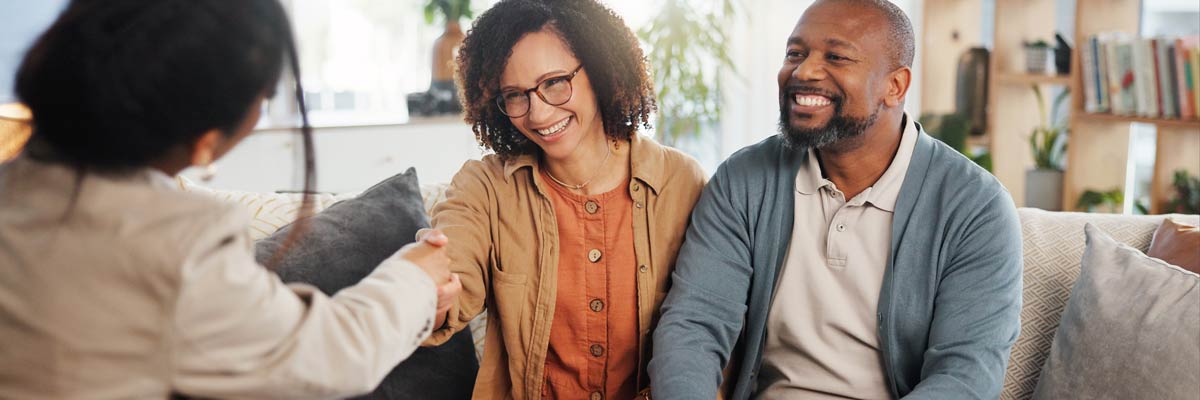 A mature couple on sofa shaking hands with a DFPI Consumer Services Officer